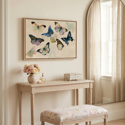 a light-colored wooden table with a vase of flowers, a small box, and a mirror above it. The table is situated in a room with a window and a painting of colorful butterflies hanging on the wall.