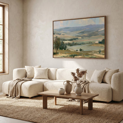 a cozy living room with a large painting of a countryside landscape hanging on the wall above a white sofa. The sofa is positioned in front of a wooden coffee table, which has a vase of flowers and a small white pitcher on it. The room has a neutral color scheme with beige walls and a brown rug, creating a warm and inviting atmosphere.