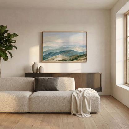 a serene living room with a large, framed landscape painting hanging on the wall above a beige sofa. The sofa is adorned with a gray throw blanket and a white vase, adding a touch of elegance to the space. A potted plant is also present, contributing to the natural and calming atmosphere of the room.