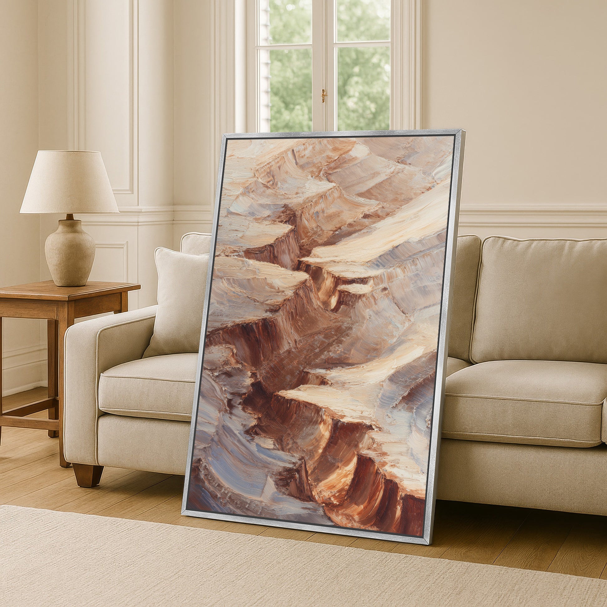 a large framed painting of a rocky landscape, with a beige sofa and a wooden side table in the background.
