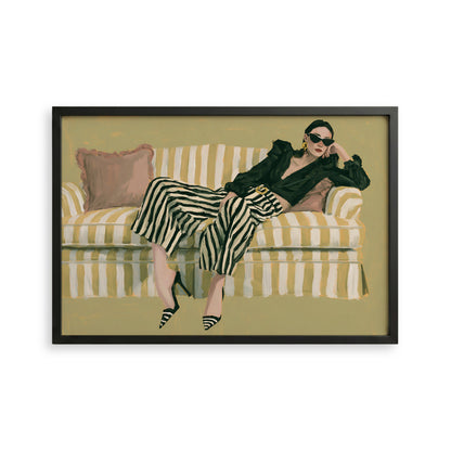 A woman is sitting on a striped couch, wearing a black jacket, striped pants, and high heels.