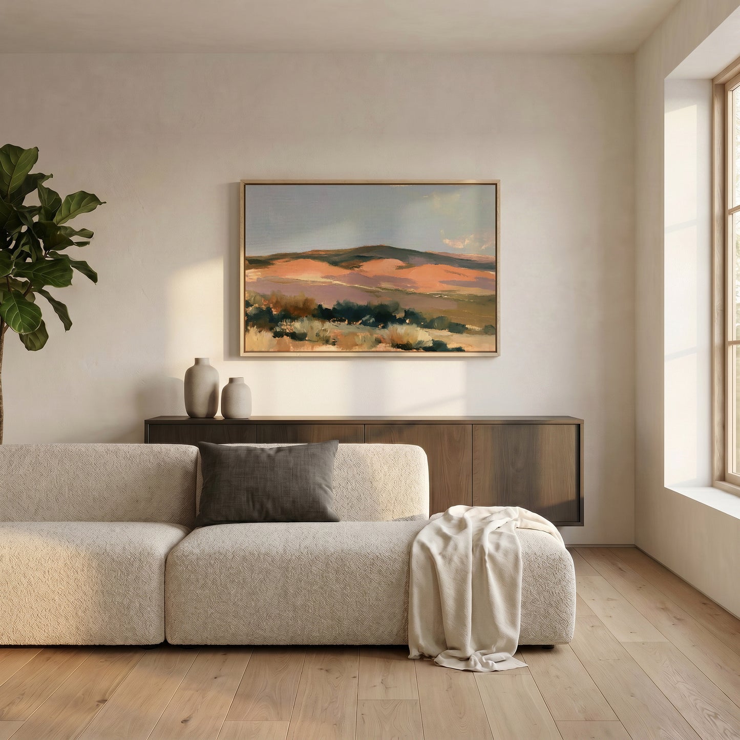 a serene living room with a large, vibrant landscape painting hanging on the wall above a beige sofa. The sofa is adorned with a gray throw blanket and a white vase, adding a touch of elegance to the space. A potted plant is also present, contributing to the natural and calming atmosphere of the room.