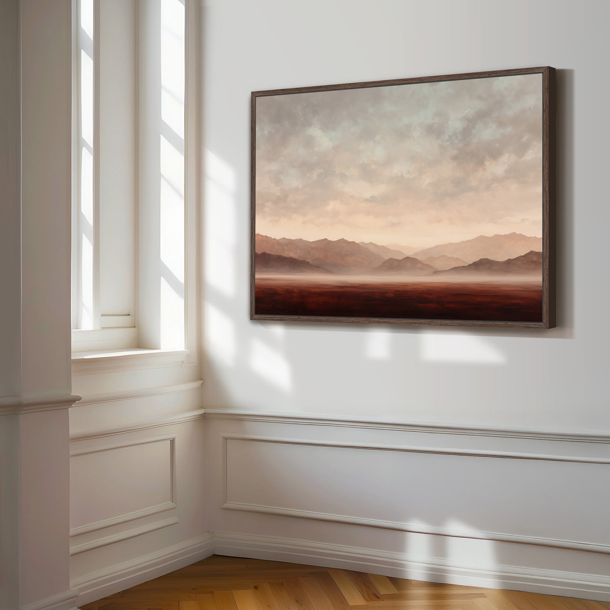 a large, framed painting of a landscape with mountains and a hazy, golden sky hanging on a white wall.