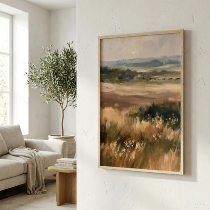 a living room with a large painting of a field of tall grass hanging on the wall. The painting is framed in a wooden frame and appears to be an oil painting. In the background, there is a couch and a potted plant, creating a cozy and inviting atmosphere.