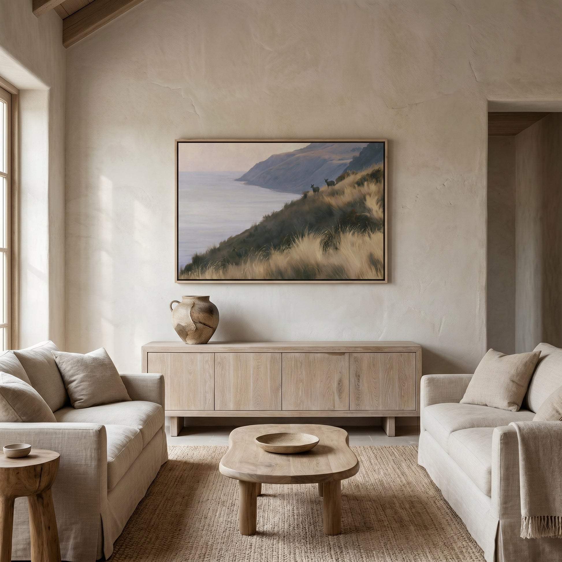 a serene living room with a large painting of a coastal landscape hanging on the wall. The room is furnished with two beige sofas and a wooden coffee table, creating a cozy and inviting atmosphere.