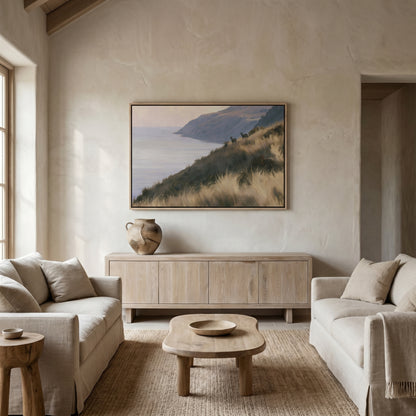 a serene living room with a large painting of a coastal landscape hanging on the wall. The room is furnished with two beige sofas and a wooden coffee table, creating a cozy and inviting atmosphere.