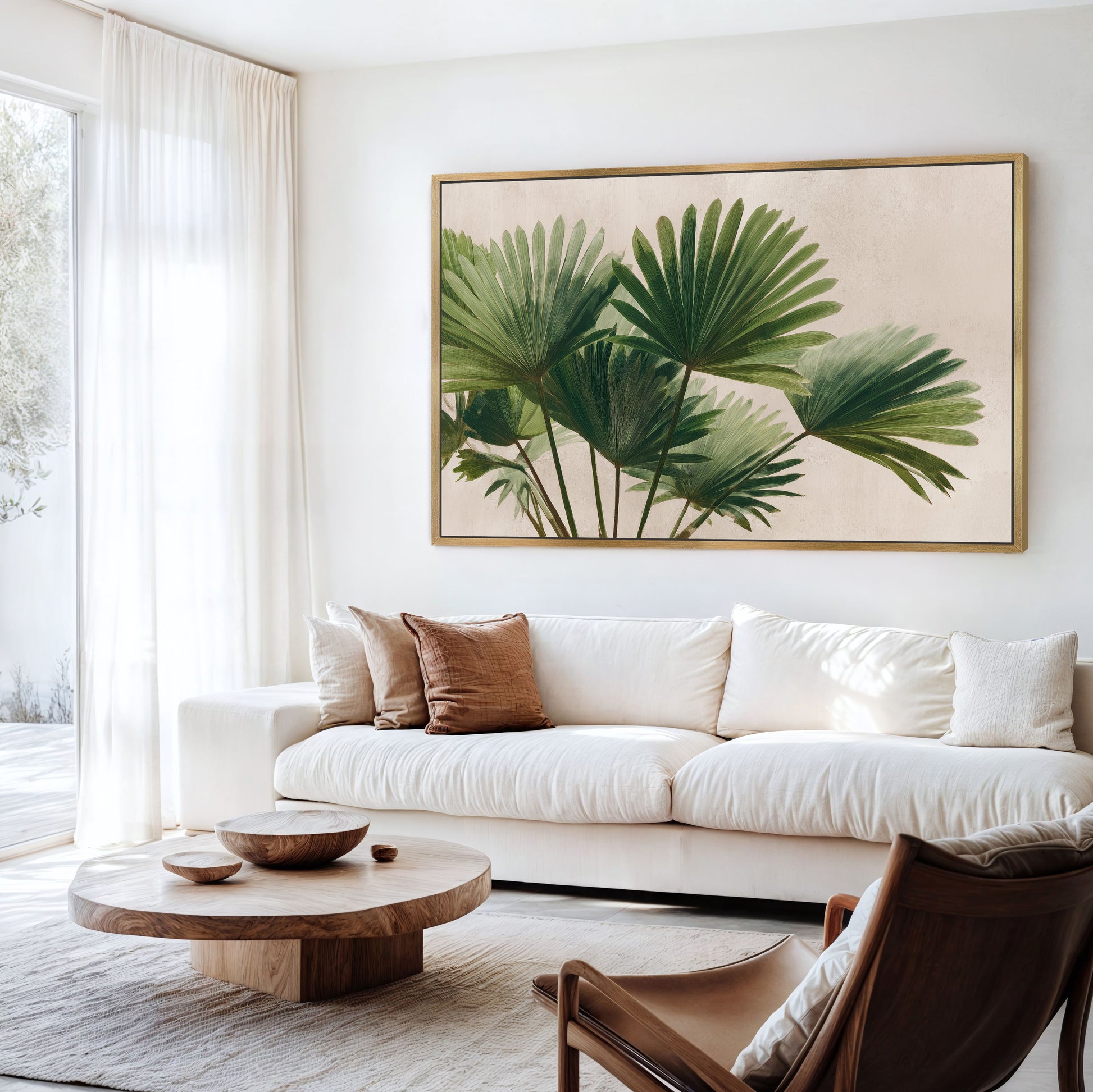 a living room with a large framed print of palm leaves on the wall, a white sofa, a wooden coffee table, and a brown leather armchair.