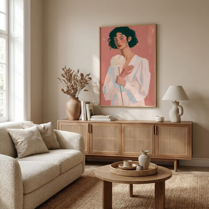 a cozy living room with a large framed painting of a woman holding a flower on the wall. The room is furnished with a beige sofa, a wooden sideboard, and a round coffee table. There are also some decorative elements such as a vase, a lamp, and a book on the sideboard.