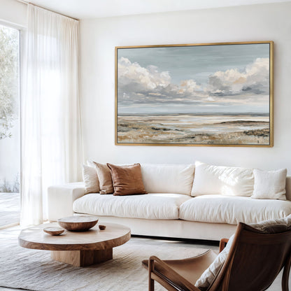 a serene living room with a large painting of a cloudy sky hanging on the wall above a white sofa. The room is furnished with a wooden coffee table, a brown armchair, and a wooden side table. The overall decor has a minimalist and modern aesthetic.