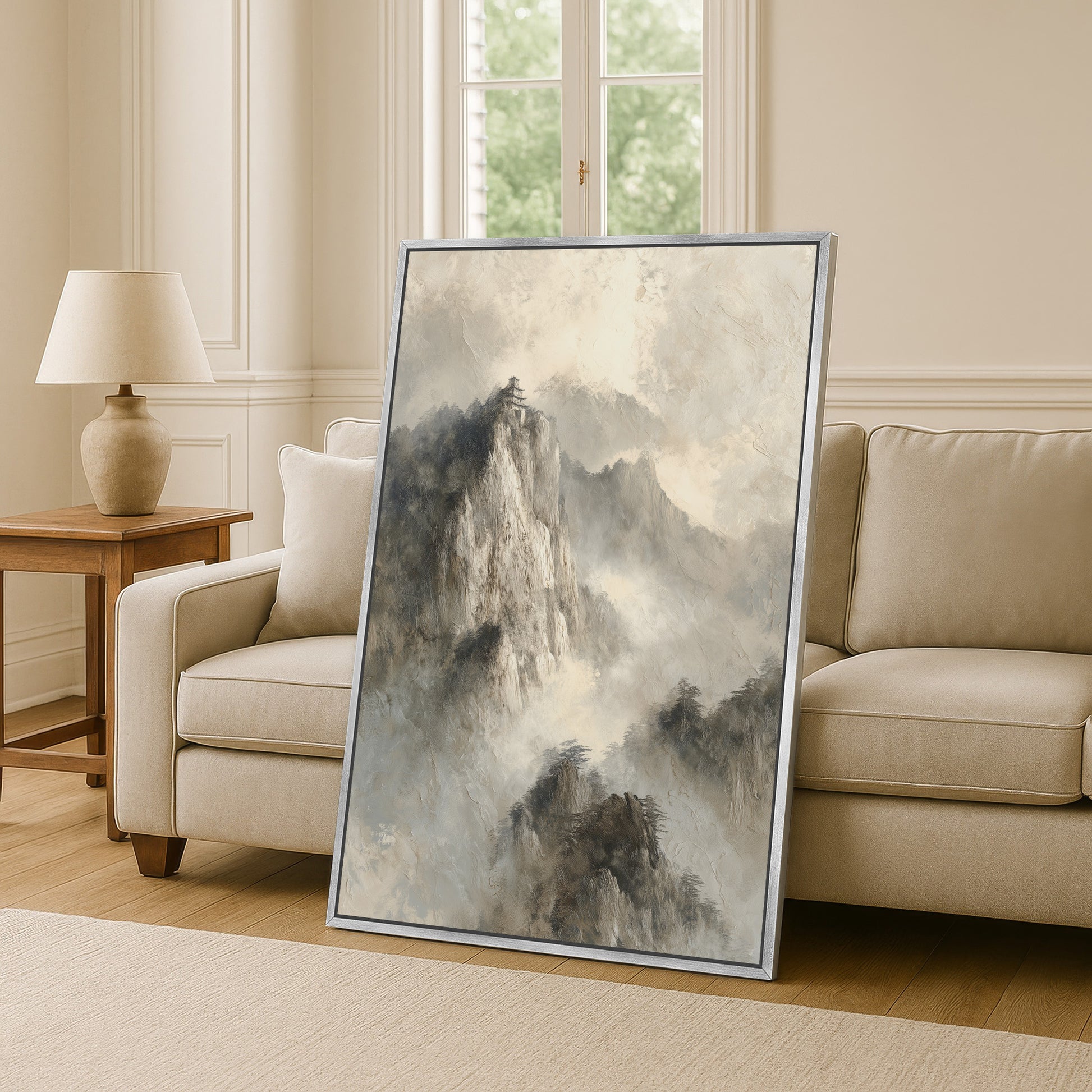 a large, framed painting of a mountainous landscape, with a cloudy sky and a temple-like structure visible in the background. The painting is placed on a wooden floor in a living room setting, with a couch and a lamp visible in the background.