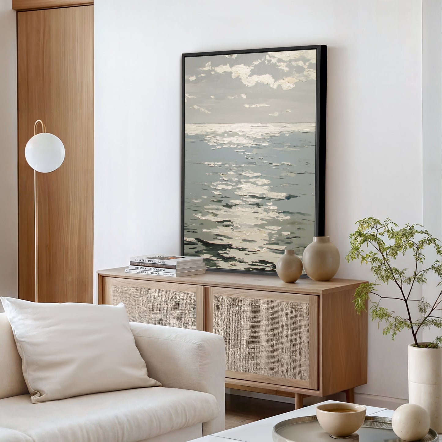 a modern living room with a large framed artwork of a seascape hanging on the wall above a wooden cabinet. The room is furnished with a white sofa, a coffee table, and a potted plant, creating a serene and inviting atmosphere.