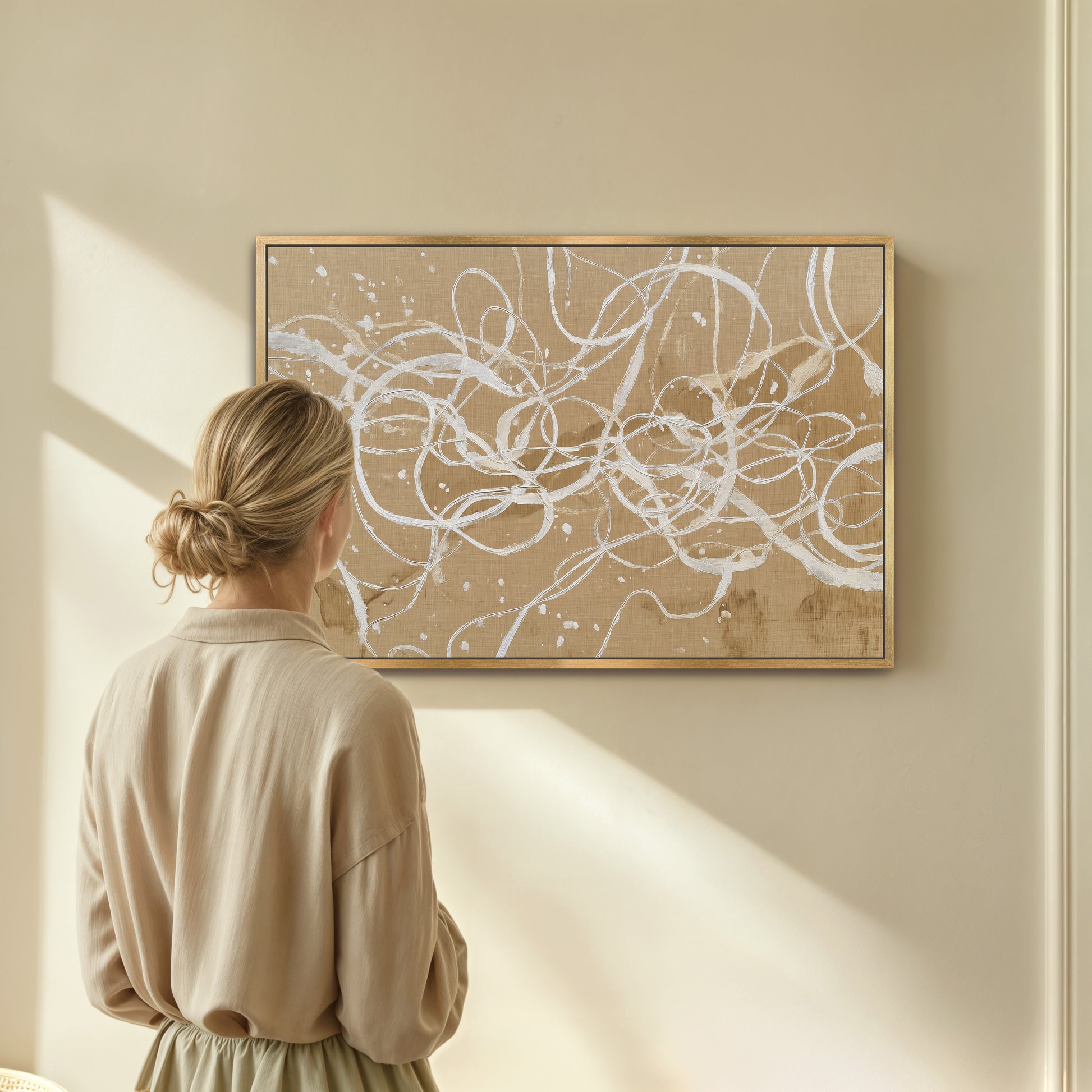 Woman admiring abstract ivory linework canvas in natural wood frame
