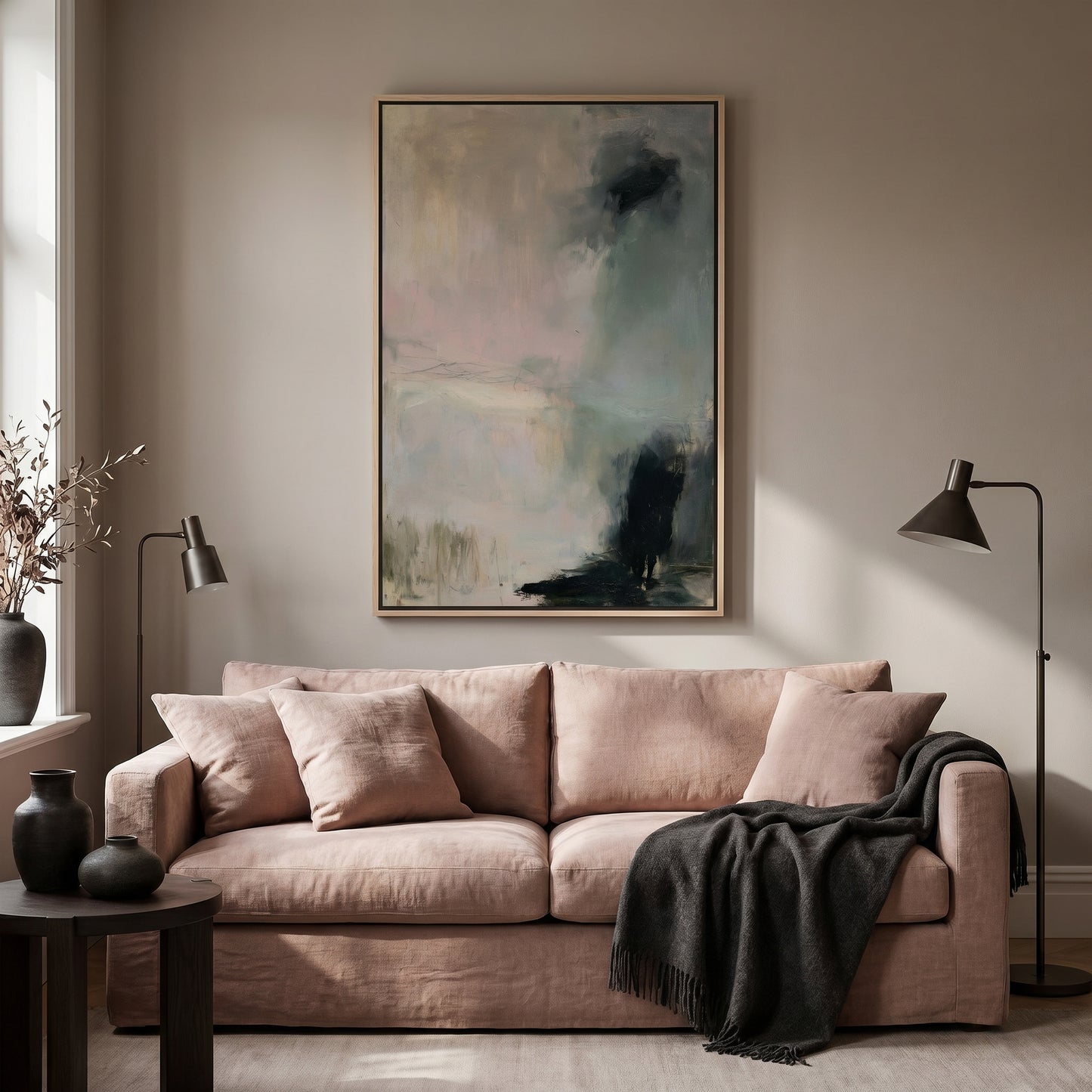 a living room with a large abstract painting hanging on the wall above a pink sofa. The sofa is adorned with a black throw blanket and has two floor lamps on either side of it. The room has a neutral color palette with a touch of gray and beige tones, creating a calm and inviting atmosphere.
