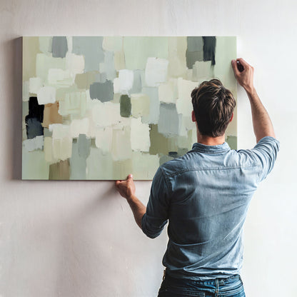 A man is hanging a large abstract painting on a wall.