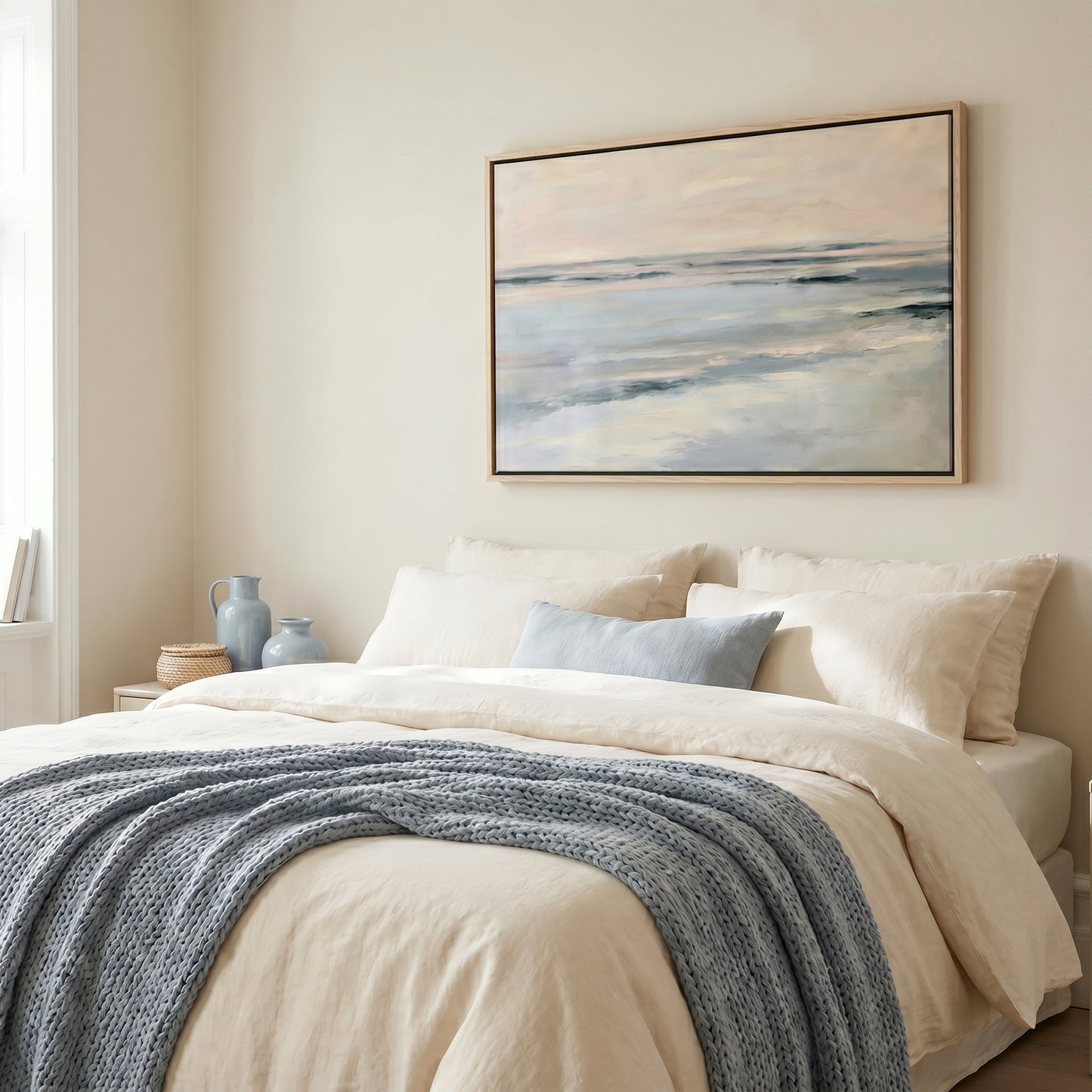 a serene bedroom scene with a large bed adorned with a blue blanket and white pillows, a framed painting of a tranquil ocean landscape hanging on the wall above the bed, and a window providing natural light to the space.
