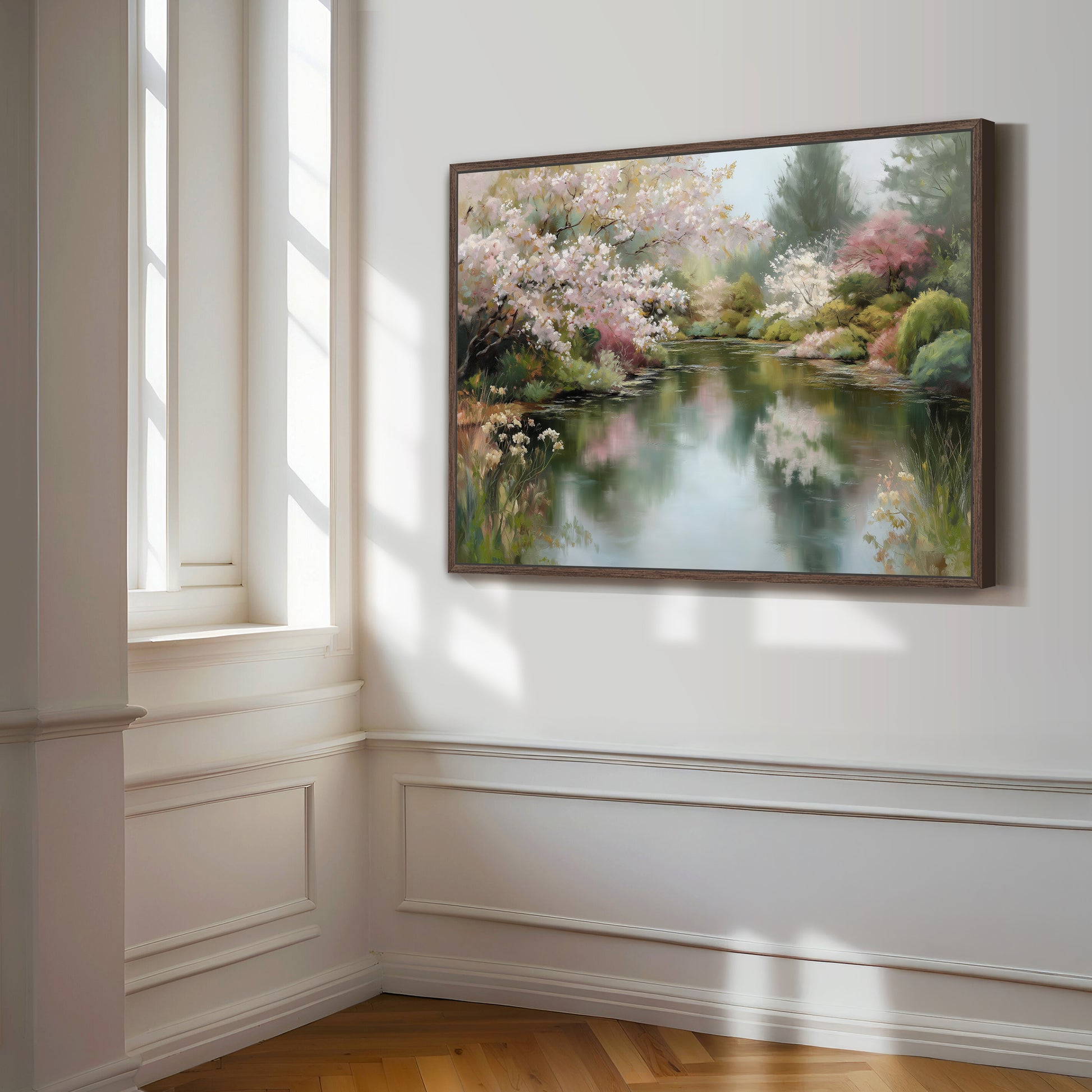 a large, framed painting of a serene landscape with a pond and blooming trees, hanging on a white wall in a room with a window.