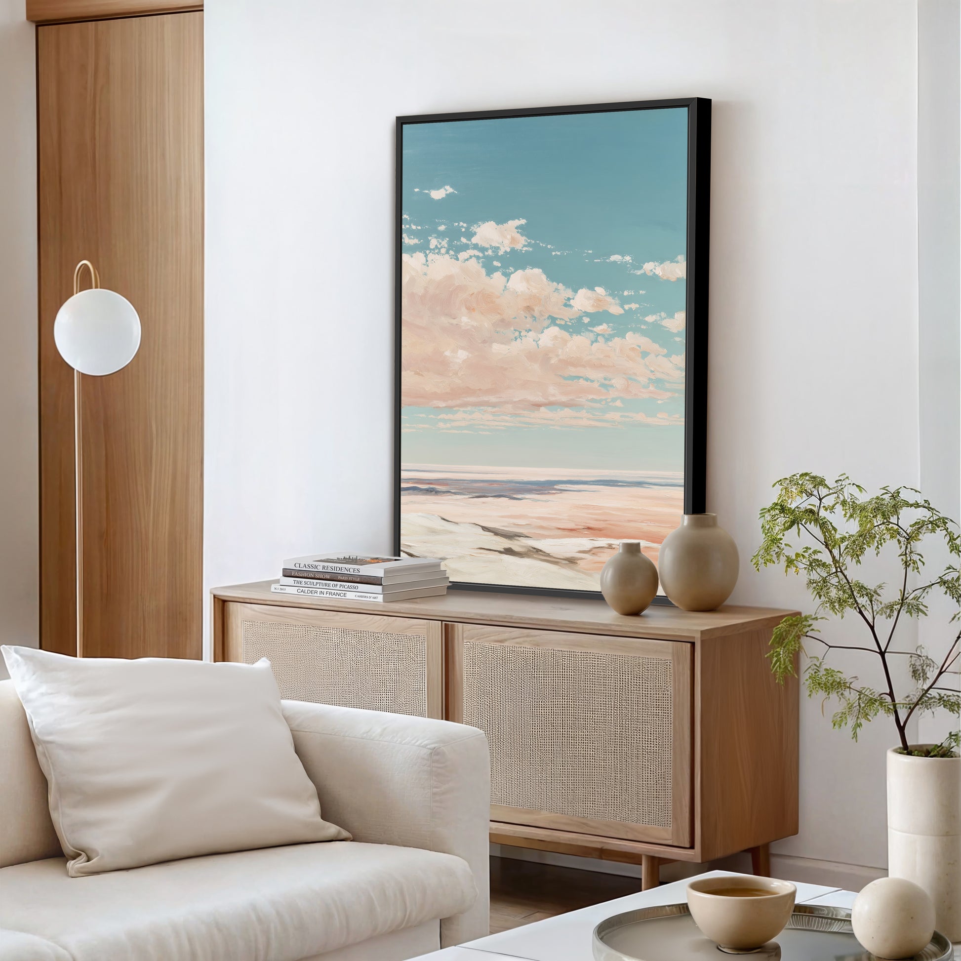 a modern living room with a large framed landscape painting hanging on the wall, a white sofa, a wooden cabinet, and a potted plant.