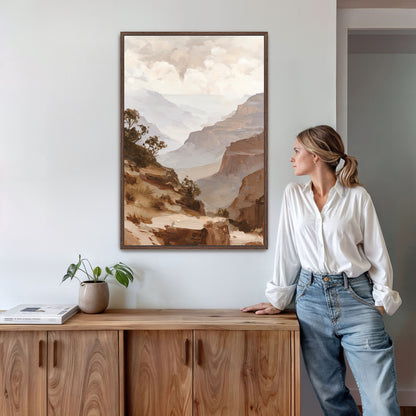 A woman in a white blouse and blue jeans stands in a room, leaning against a wooden cabinet, with a framed landscape painting hanging on the wall behind her.