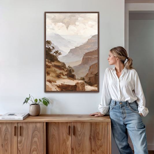 A woman in a white blouse and blue jeans stands in a room, leaning against a wooden cabinet, with a framed landscape painting hanging on the wall behind her.