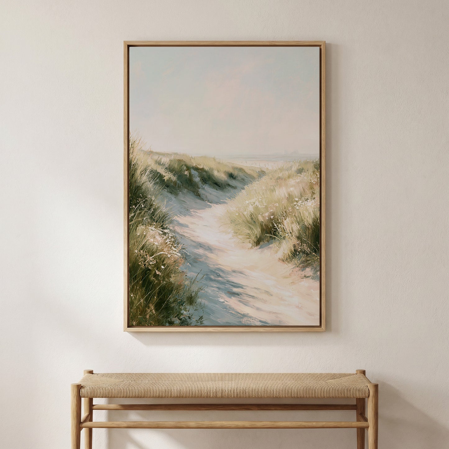a large framed painting of a sandy path leading through a grassy field, hanging on a wall above a wooden bench.