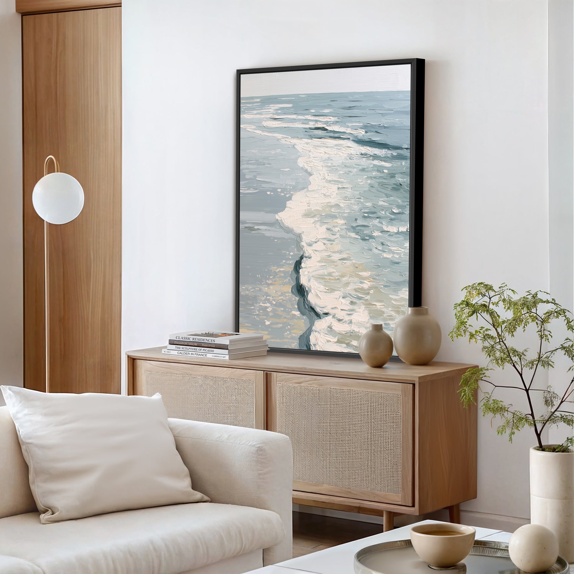 a serene living room with a large painting of a tranquil ocean scene hanging on the wall above a wooden cabinet. The room is furnished with a white sofa, a coffee table, and a potted plant, creating a cozy and inviting atmosphere.