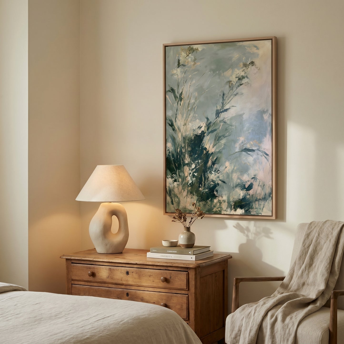 a serene and cozy bedroom scene, featuring a wooden dresser with a lamp, a framed painting of a lush green plant, and a comfortable chair.