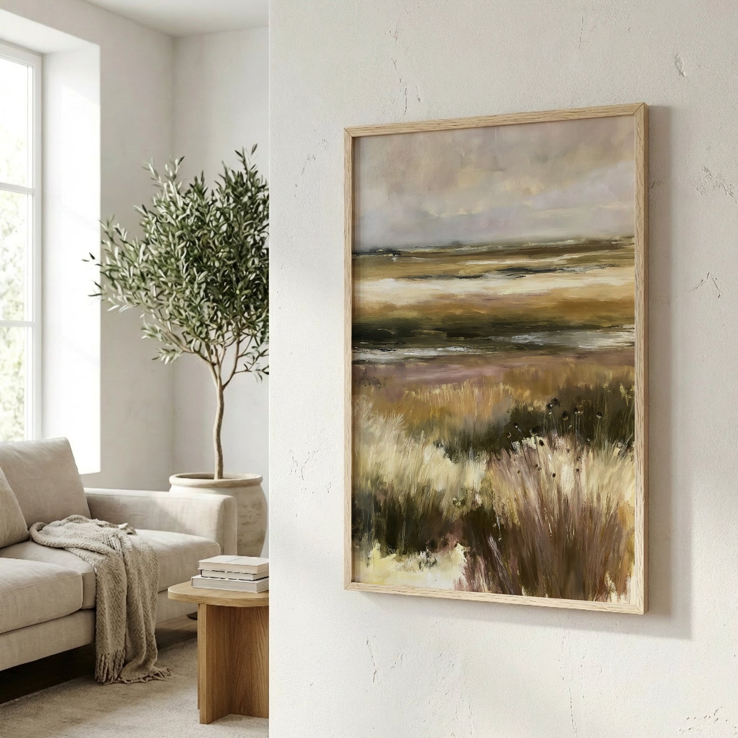 a living room with a large painting of a field of tall grass hanging on the wall. The painting is framed in a wooden frame and appears to be a landscape artwork. In the background, there is a window that allows natural light to enter the room, and a potted plant is visible on the left side of the image.