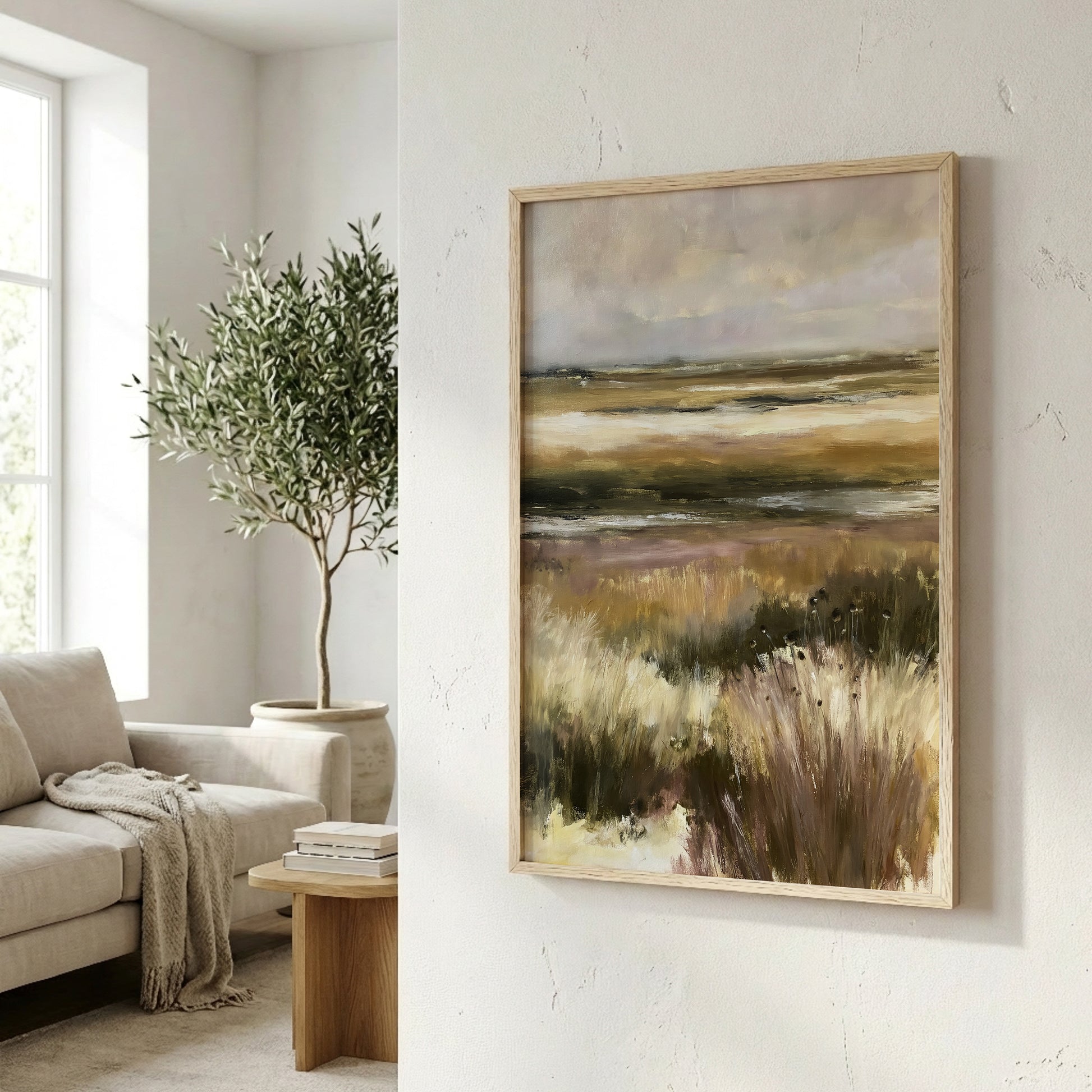 a living room with a large painting of a field of tall grass hanging on the wall. The painting is framed in a wooden frame and appears to be a landscape artwork. In the background, there is a window that allows natural light to enter the room, and a potted plant is visible on the left side of the image.