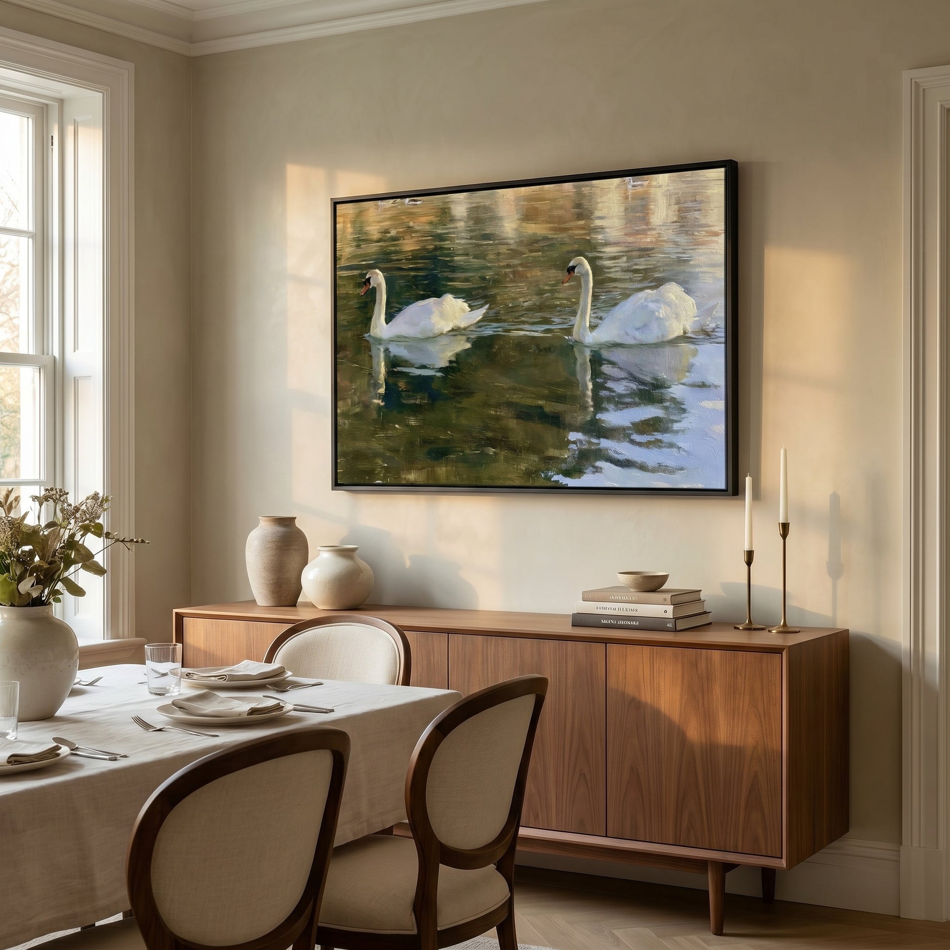 a serene dining room with a large framed painting of two swans swimming on a calm body of water hanging on the wall above a wooden cabinet. The dining table is set with plates, bowls, and a vase of flowers, creating a cozy and inviting atmosphere.