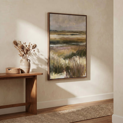 a large landscape painting hanging on a wall, with a wooden table and a woven basket nearby. The painting depicts a serene countryside scene with rolling hills and a field of tall grass.