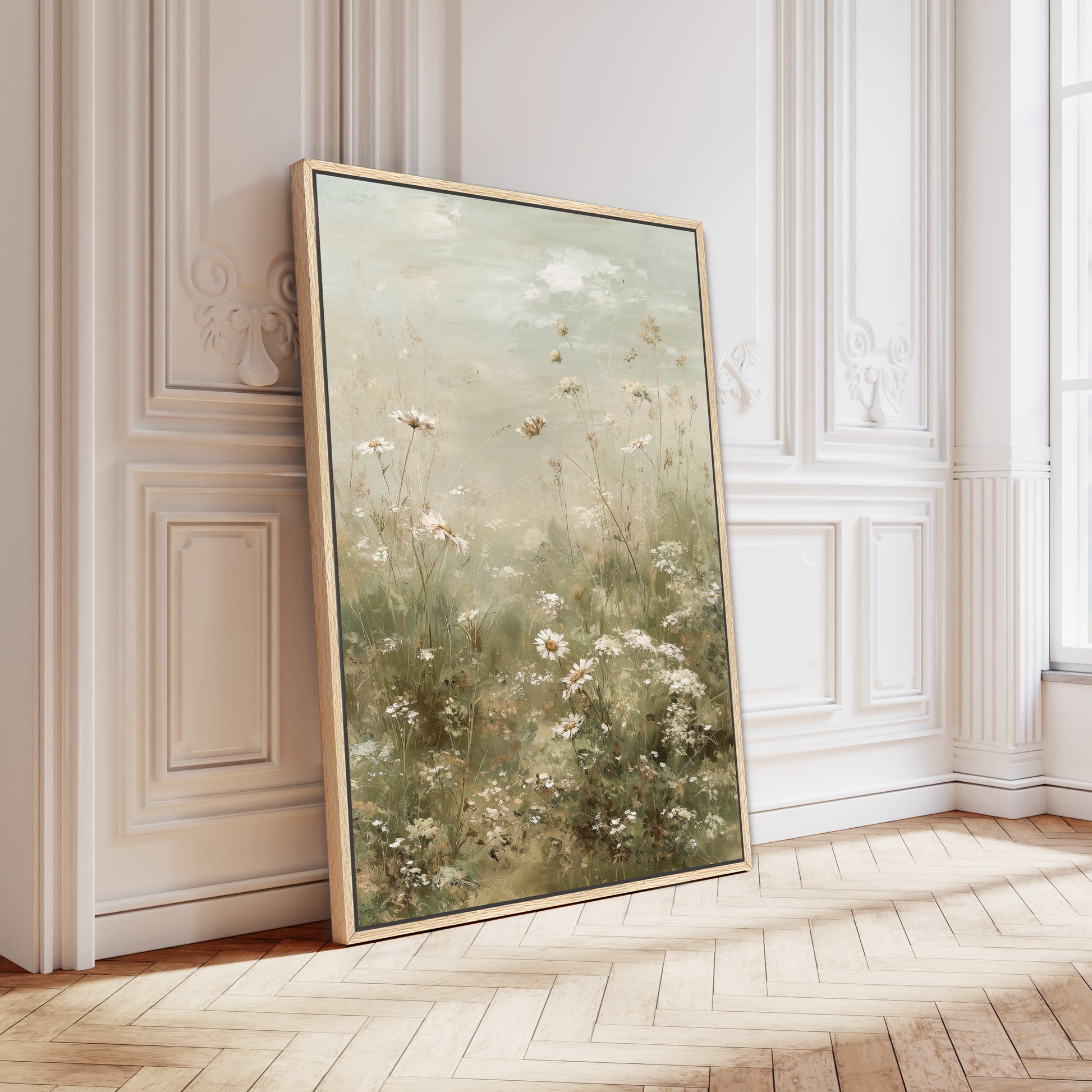 a large framed painting of a field of flowers, leaning against a white wall in a room with a wooden floor.