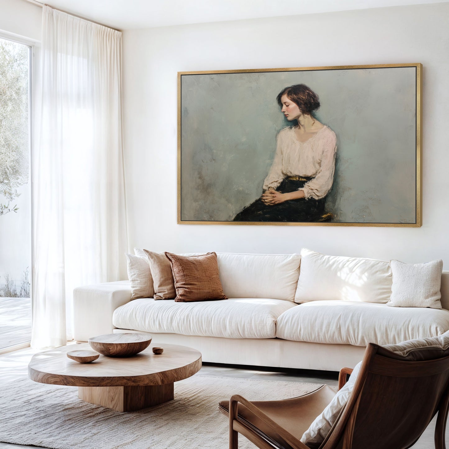 Elegant contemplative portrait in a gold frame hanging above a white sofa in a bright living room with natural wood accents.
