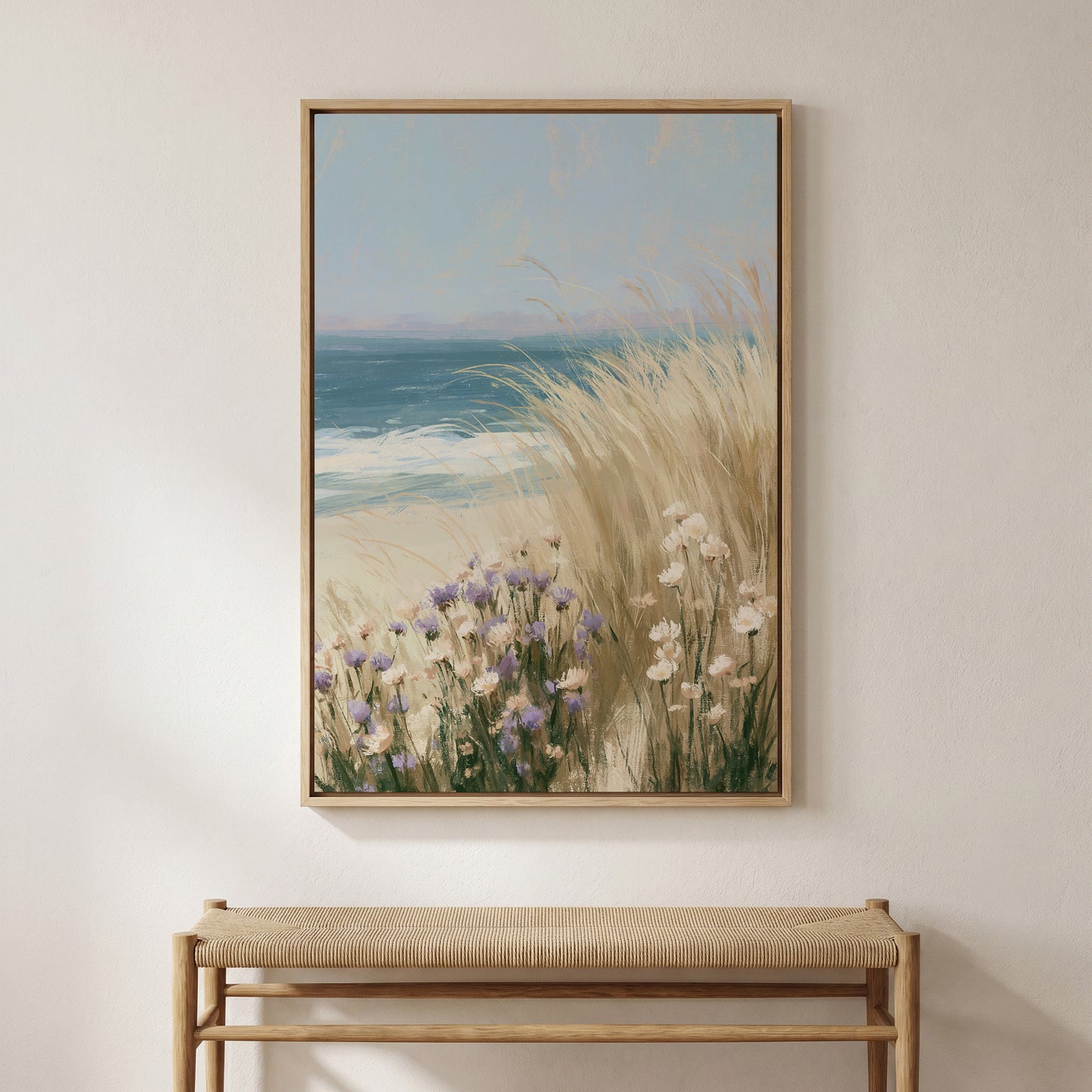 a large framed painting of a beach scene with tall grasses and flowers, hanging on a wall above a wooden bench.