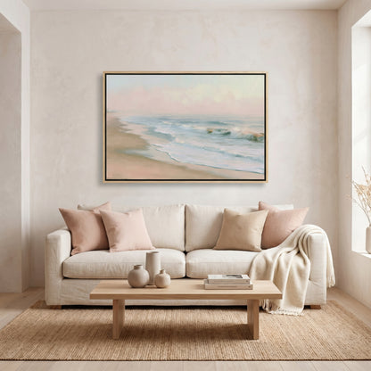 a living room with a large painting of a beach scene hanging on the wall above a white sofa with beige pillows. The sofa is positioned in front of a wooden coffee table, which has a vase and a book on it. The room has a neutral color scheme with beige walls and a wooden floor, creating a calm and inviting atmosphere.