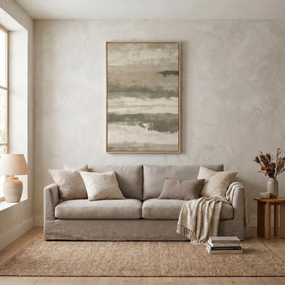a cozy living room with a large window, a gray sofa adorned with throw pillows, and a framed abstract painting hanging on the wall above the sofa.