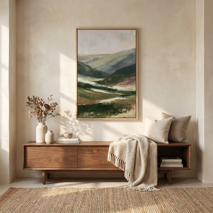 a serene and cozy living room setting with a large painting of a mountain landscape hanging on the wall above a wooden console table. The table is adorned with a vase of dried flowers, a stack of books, and a beige throw blanket. The room has a warm and inviting atmosphere, with natural light streaming in from a window on the left side.