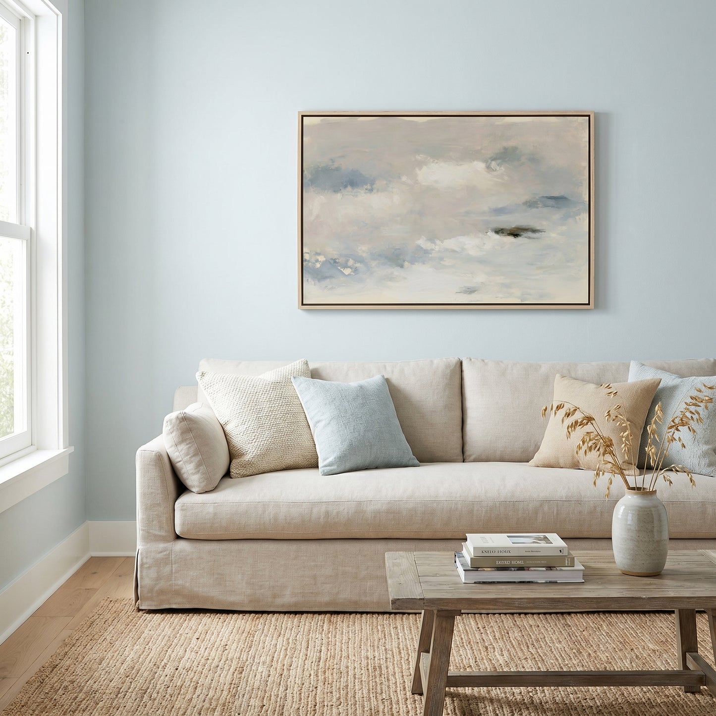 a cozy living room with a beige sofa adorned with throw pillows, a wooden coffee table, and a framed landscape painting hanging on the wall above the sofa.