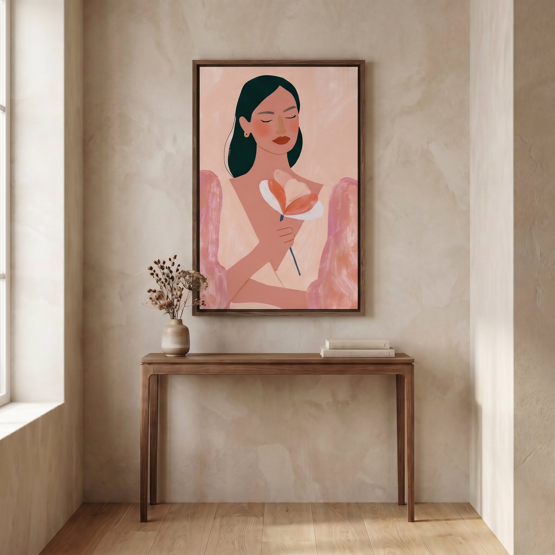 a wooden console table with a vase of flowers and a stack of books on it, set against a light-colored wall. Above the table, there is a framed illustration of a woman holding a flower.