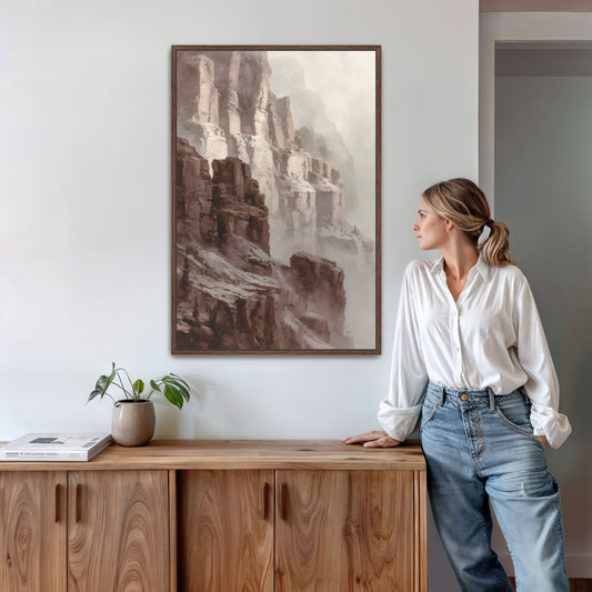 Canyon cliff wall art in brown frame above wooden sideboard with woman standing beside.