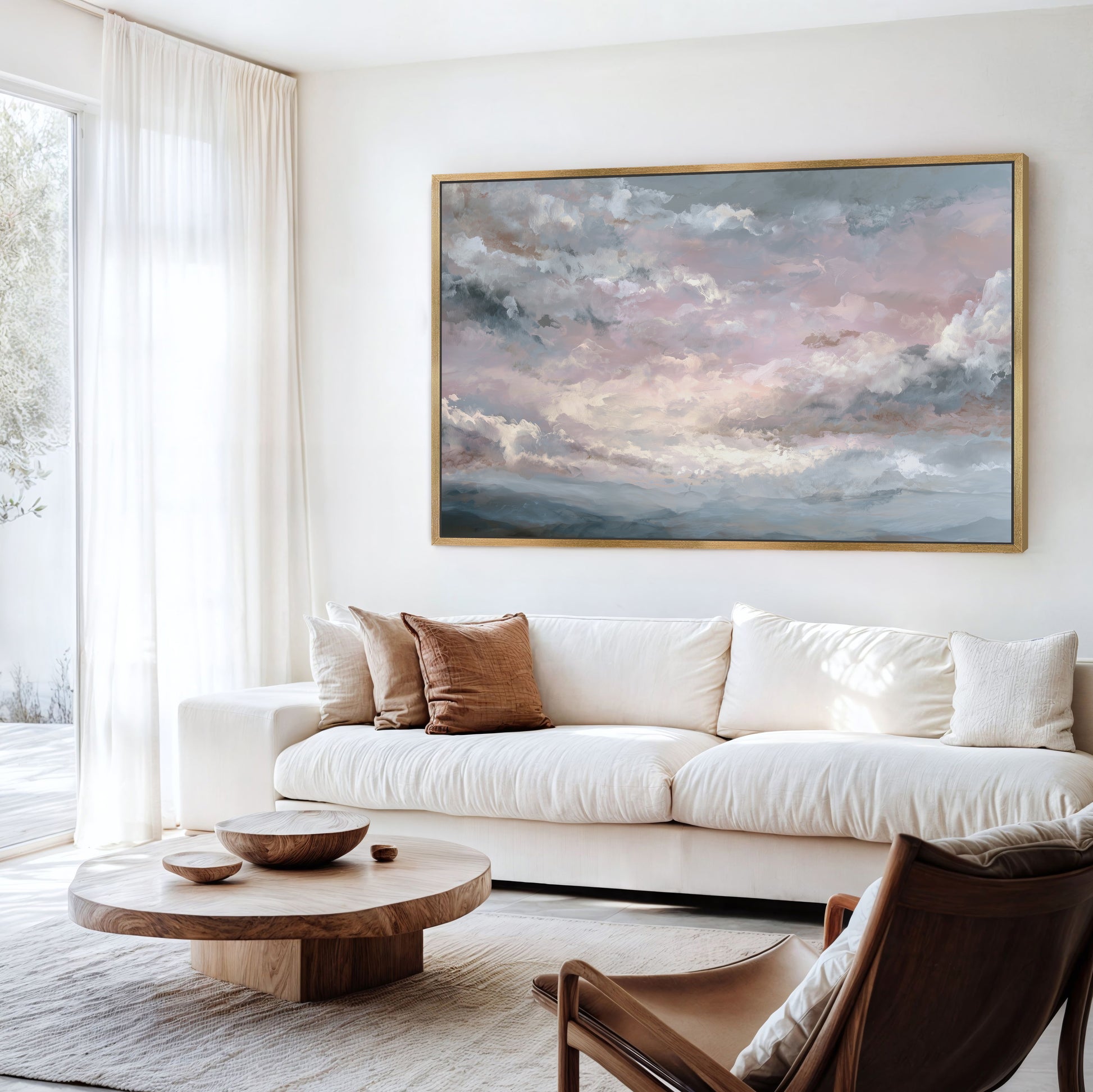 Pink sky and clouds artwork in a gold frame above a neutral sofa.