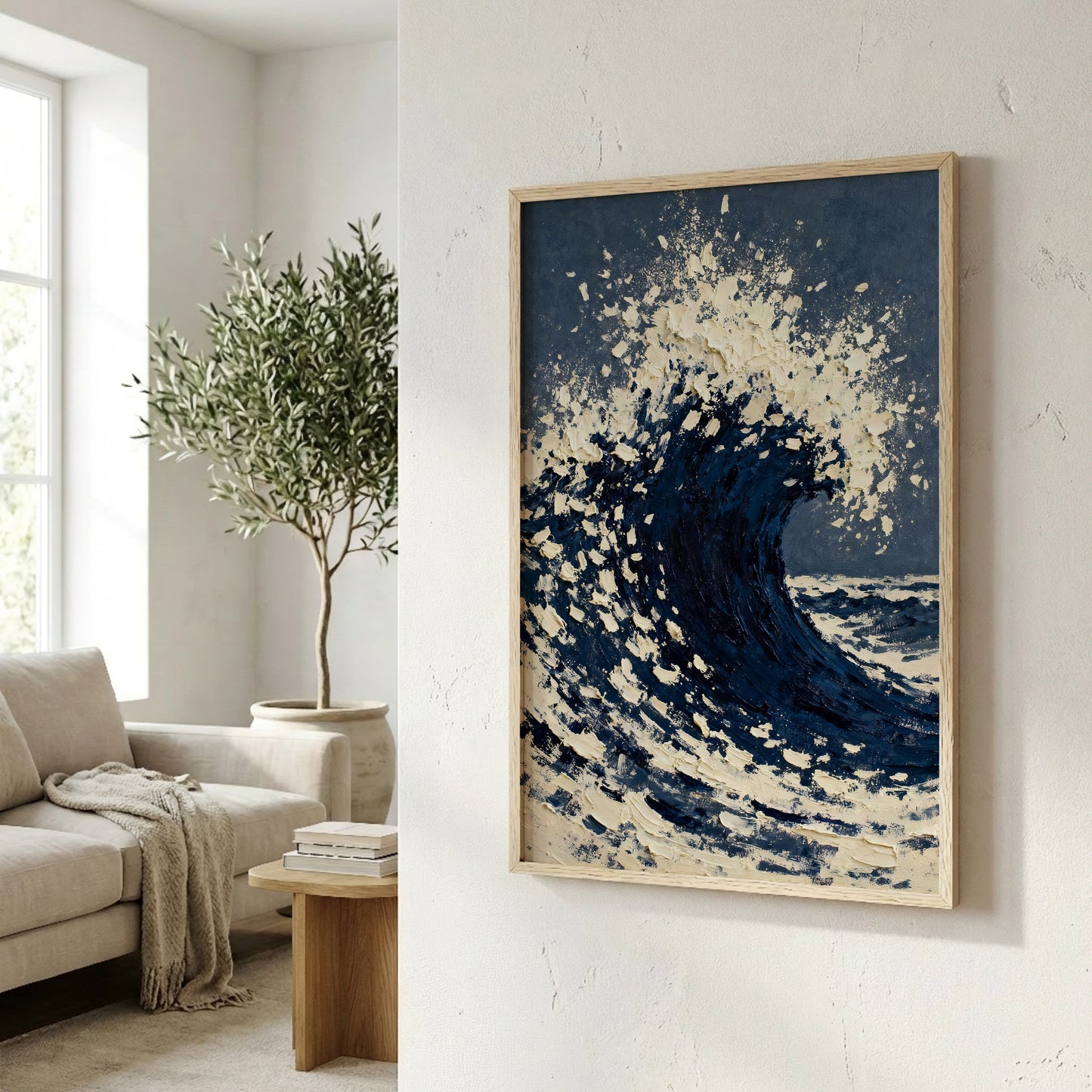 a large framed painting of a crashing wave, hanging on a wall in a living room. The painting is predominantly blue and white, with splashes of white creating a sense of movement and energy. In the background, there is a window with a tree outside, adding a natural element to the scene. The room also contains a couch, a coffee table, and some books, creating a cozy and inviting atmosphere.