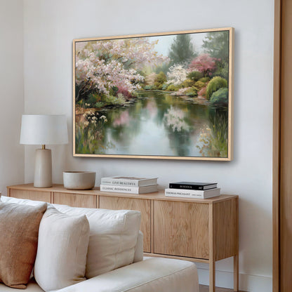 a large painting of a serene landscape with a pond and blooming trees, hanging on a wall above a wooden cabinet with books and a lamp.