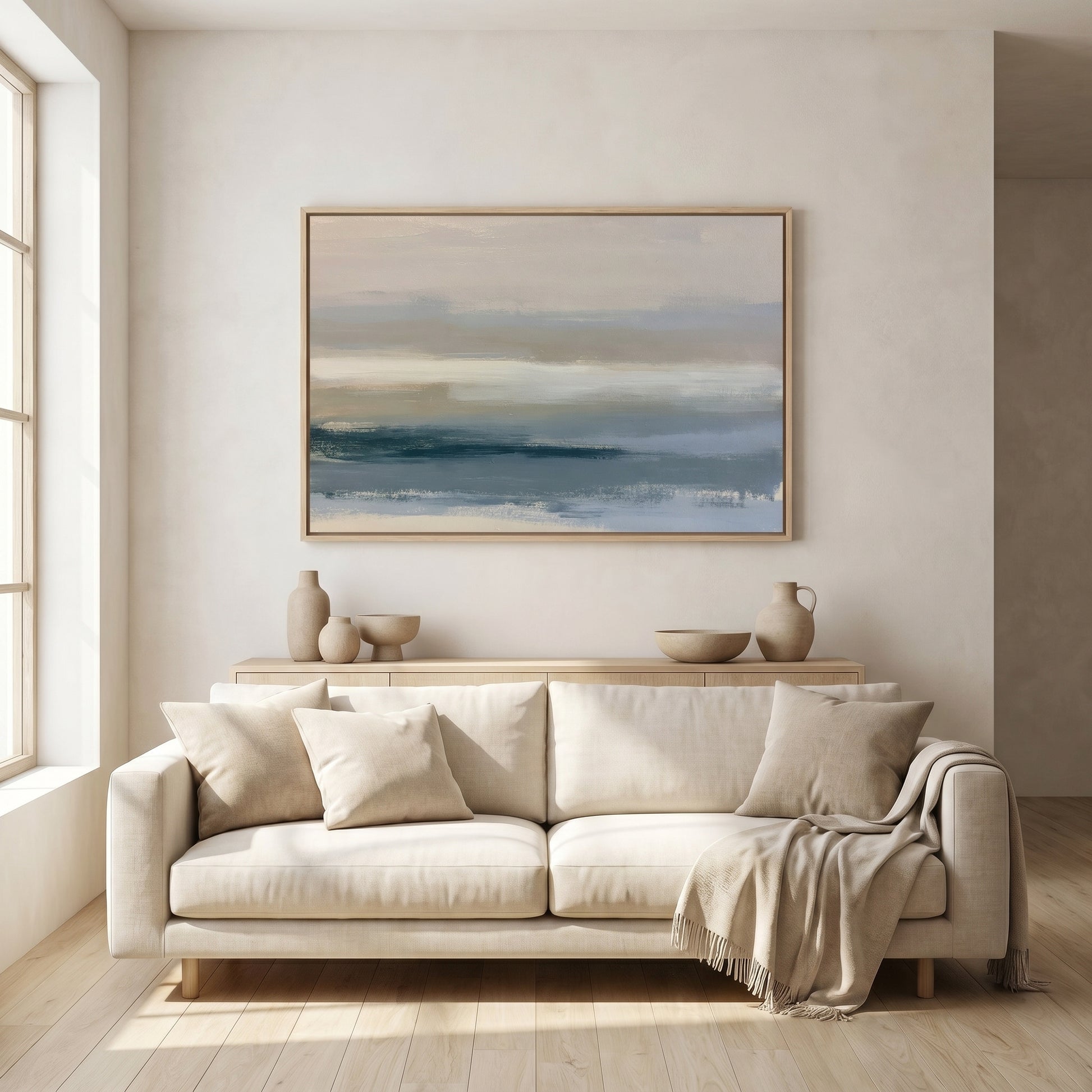a large, light-colored sofa with a beige throw blanket draped over it, positioned in front of a large, framed painting depicting a serene landscape.