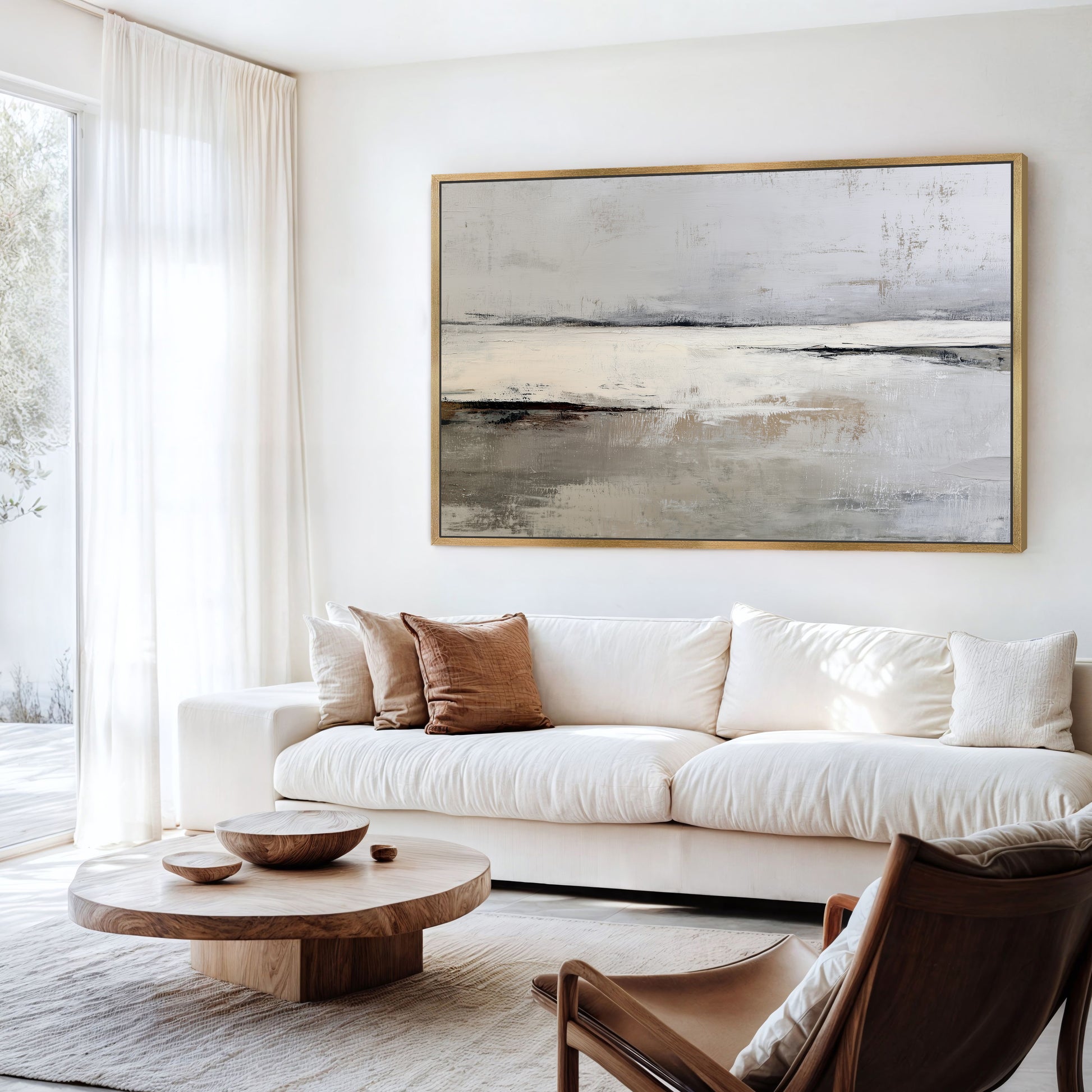 a modern living room with a large abstract painting hanging on the wall above a white sofa. The room is furnished with a wooden coffee table, a brown leather armchair, and a wooden side table. The overall color scheme and design of the room create a serene and contemporary atmosphere.
