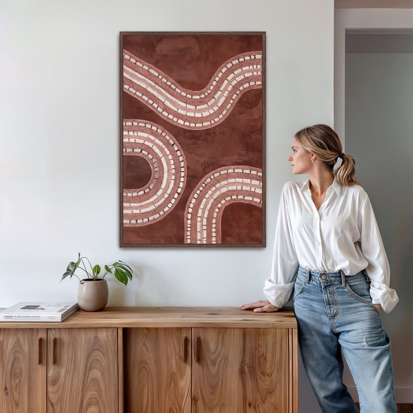 Woman standing next to a wooden cabinet with a large abstract painting on the wall.