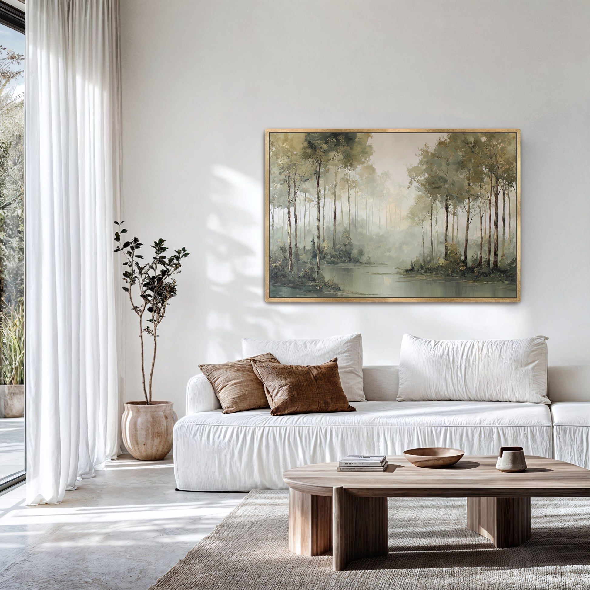 Misty forest edge landscape print in a natural frame above a white sofa in a light-filled room.