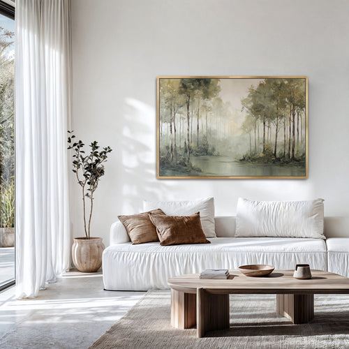 Misty forest edge landscape print in a natural frame above a white sofa in a light-filled room.