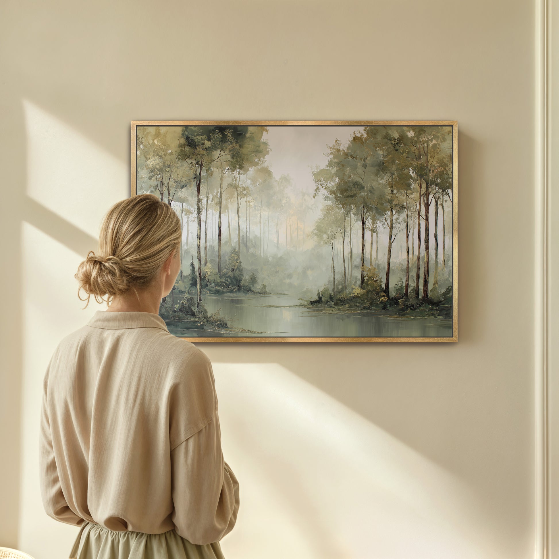 Woman admiring a misty forest edge framed wall art in a softly lit room.