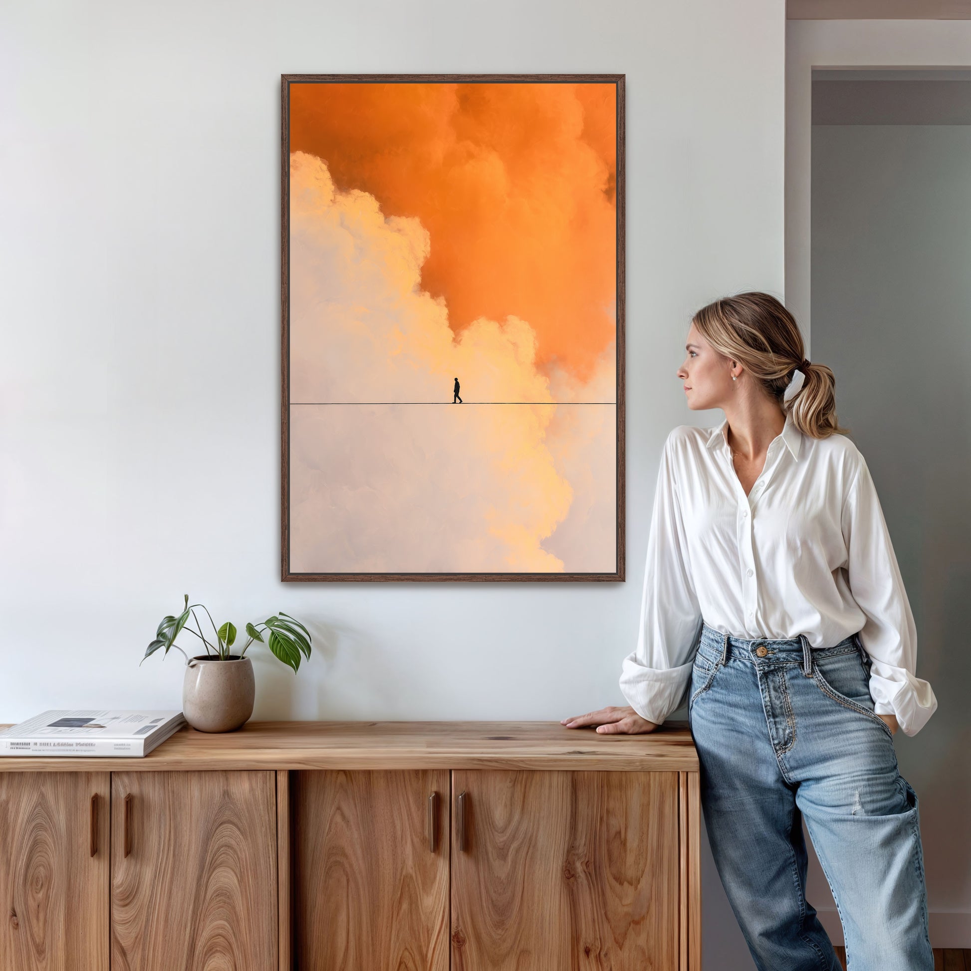 Contemporary home interior with woman standing beside large framed orange cloud art above console table