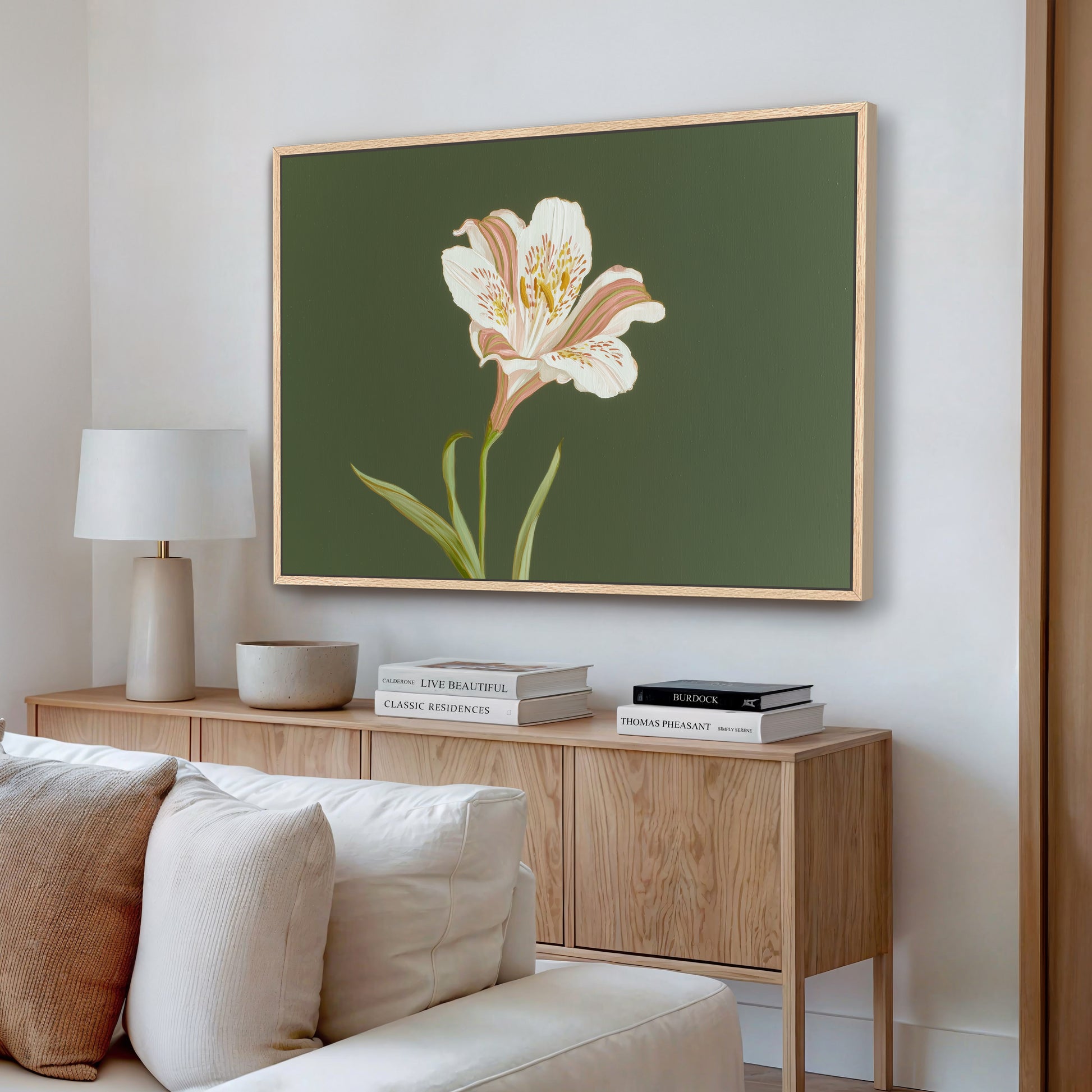 White lily floral canvas wall art on green background styled above a wooden console with lamp and books